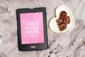 Kindle on Bed Next to Sweets Mockup Generator