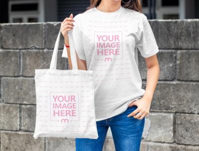 Mockup of a Shirt and Tote Bag Featuring a Woman Sand in Front of a Stone Wall